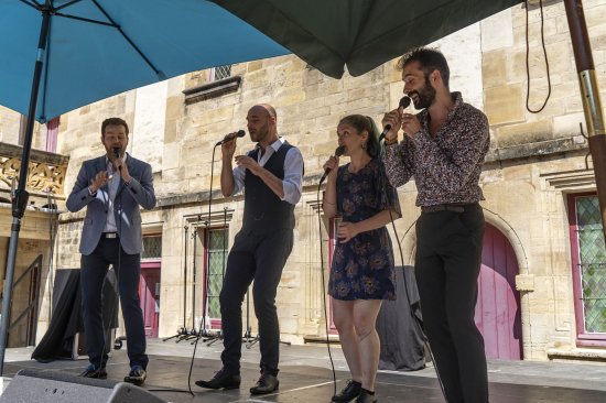 Photo de groupe, sur la scène du collège Gilles de Trèves, des 4 chanteurs de Climax micro à la main et abrités du soleil par deux parasols.