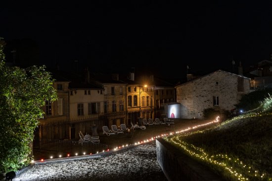 Festival Bar'Envoix 2023 Jardin Collège Gilles de Trêves. Eclairage décoratif de guirlandes de lucioles et ampoules rouges et blanches. Dans le fond, quelques chaises longues permettent aux festivaliers de se reposer.