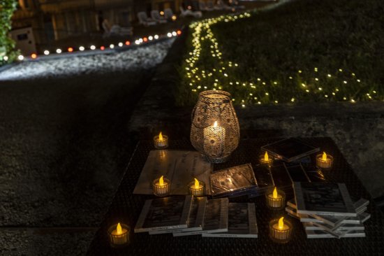 After Festival Bar'Envoix 2023 Jardin Collège Gilles de Trêves. Une table éclairée d'un ambiance douce de bougies led expose les CD du groupe Slixs. L'arrière plan montre un jardin éclairé de centaines de lucioles.