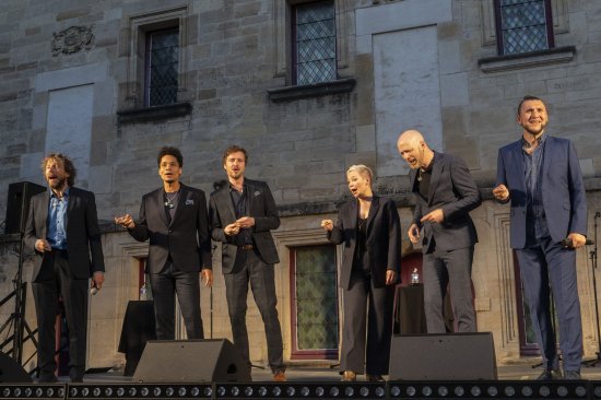 Les 6 membres du groupe Slixs en train de chanter devant un mur éclairé de blanc