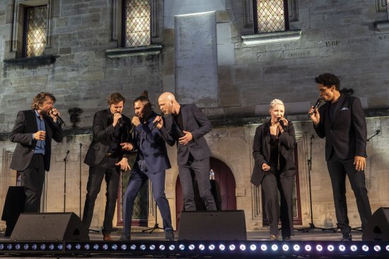 Les 6 membres du groupe Slixs en train de chanter devant un mur éclairé de blanc