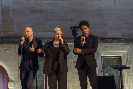 3 membres du groupe Slixs en train de chanter devant un mur éclairé de blanc