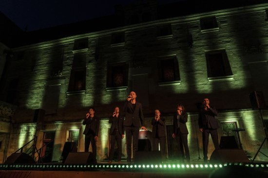 Les 6 membres du groupe Slixs sur scène devant un mur éclairé de bandes verticales de lumières vertes