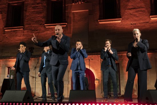 Photo des 6 artistes du groupe Slixs sur la scène du collège devant un mur éclairé de nuances de rouge et d'orange mettant en valeur portes et fenêtres.