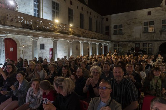 Public vu de face dans la cour Gilles de Trèves avec les coursives et les colonnades éclairées de blanc