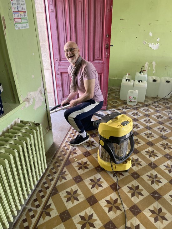 Bar'EnVoix 2023 - Photo des coulisses - Accroupi, Stéphane, hilare aspire la saleté d'une pièce du cllège