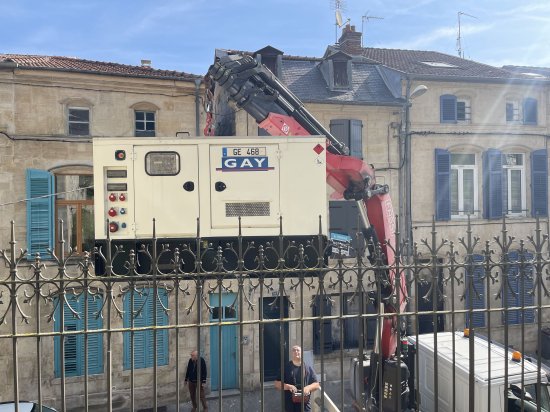 Bar'EnVoix 2023 - Photo des coulisses - Le groupe électrogène est hissé par dessus la rambarde de fer du jardin du collège Gilles de Trèves