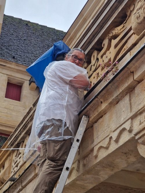 Daniel, en poncho et en haut d'une échelle, installe les lumières des coursives du collège.