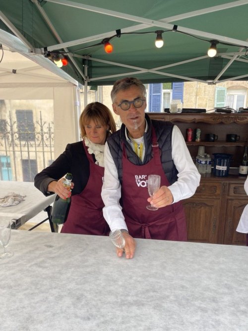 Eric et Nathalie, les deux barmen avec des tabliers Bar'EnVoix de couleur bordeaux en train de servir des coupes de champagne à la guinguette.