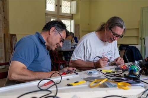 Sylvain et Daniel, attablés et fer à souder à la main, préparent les rubans de LED qui serviront à éclairer les coursives du collège