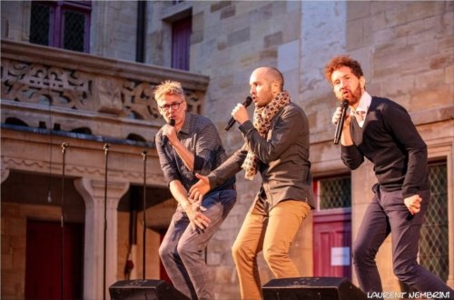 Emmanuel, Mathieu et Nicolas du groupe Opus Jam, micro à la main chantent en trio sur scène dans la cour du collège Gilles de Trèves dans le soleil couchant.