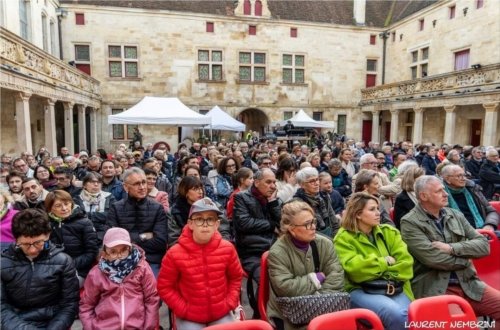 Le public 2024 assis sur des chaises dans la cour du collège Gilles de Trèves vu de la scène. On distingue la régie son et lumière dans le fond.