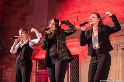 Oriane, Valentine et Véronique du groupe Just vox en train de chanter, micro à la main et faisant semblant de montrer leurs biceps avec l'autre bras.