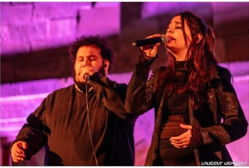 Valentine et Big Ben du groupe Just Vox, micro à la main en train de chanter devant un mur éclairé de mauve.