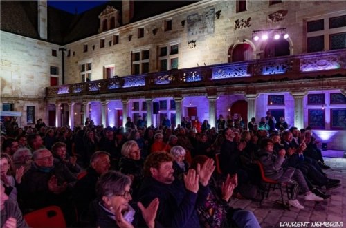 Assis, le public applaudit les artistes dans la cour du collège Gilles de Trèves avec les coursives éclairées en blanc et les arcades en violet