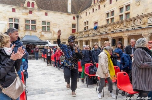 Mayiha-Ta Nguidjoe du groupeThe Sparkle Family chante parmis le public en passant dans le couloir entre deux rangées de chaises. Le publis est debout et frappe dans les mains.