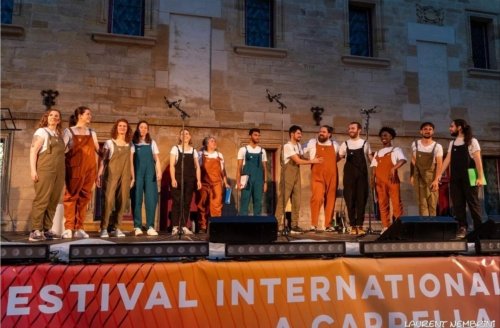 Photo de groupe, sur scène, des 13 artistes du groupe Atelier Chorale U à la fin du spectacle. La nuit commence à tomber.