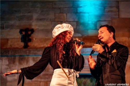 Tanya et Fabio de Mezzotono en duo. Tania est déguisée en chef de cuisine avec un tablier et une toque. Une spatule de bois dépasse de la poche de son tablier.