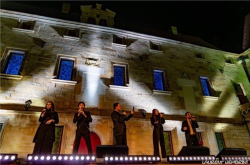 Les 5 membres du groupe Mezzotono chantent sur la scène du collège Gilles de Trèves devant une paroi éclairée de faisceaux lumineux blanc