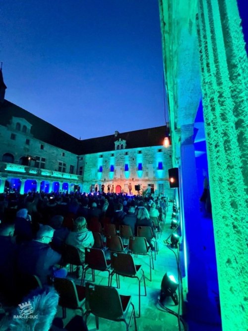 Le public vu de dos dans la cour du collège Gilles de Trèves éclairé d'une combinaison de couleurs bleues et turquoise pour mettre en avant l'architecture
