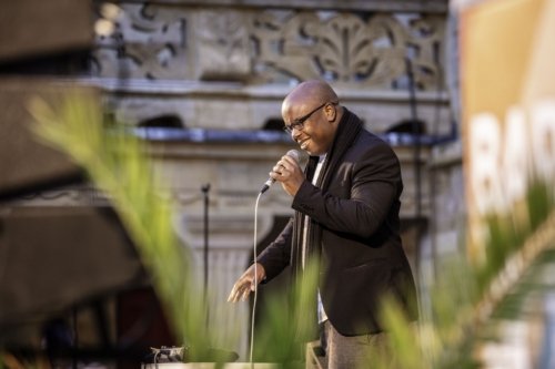 Hervé Fontaine, micro à la main fait une démonstration de beatbox. La photo est prise au travers de feuillages floutés.