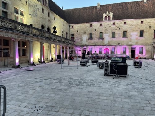 Photo d'ensemble de l'installation technique de la cour du collège Gilles de Trèves. En premier plan, les flight case, la console de régie lumière. Au fond, la scène et les murs qui commencent à êtres éclairés de mauve