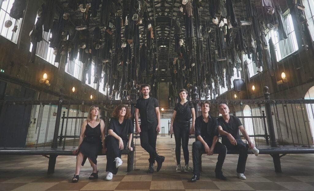 Le groupe Exeko, assis sur des bancs dans un hall tapissé de draperies noires au plafond