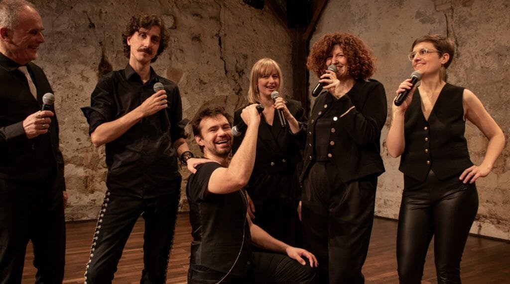 Le groupe Exeko, micro à la main, en train de poser pour la photo dans une pièce avec poutres et murs de pierre