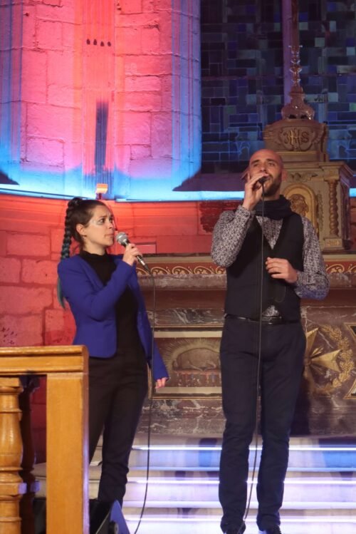 Cécile et Julien chantent micro à la main dans la nef de l'église