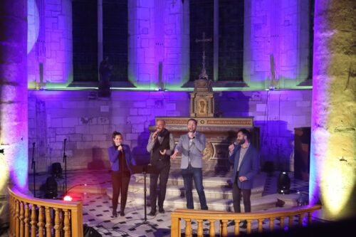 Vue en élévation du groupe ClimaX chantant dans une nef éclairée de teintes bleues et vertes