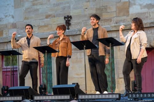 Le groupe A Bocca Chiusa devant leur pupitre chante sur la scène en claquant des doigts