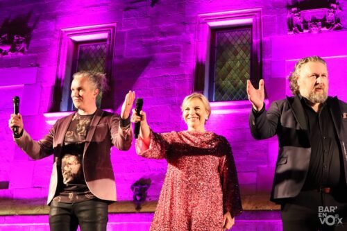 Juha, Laiji et Tuukka saluent le public devant une paroi éclairée de mauve