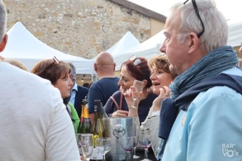 Vue des festivaliers, verre à la main, devant les bouteilles de champagne et de vin en train de discuter et passer du bon temps