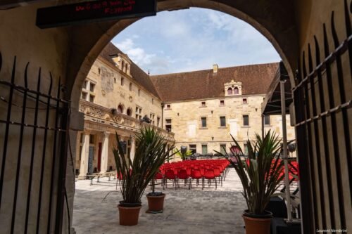 Vue du collège Gilles de Trèves depuis la voûte d'entrée. Les chaises rouges alignées, la scène au fond et des plantes en premier plan.