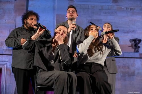 Les chanteurs de JustVox, regroupés, chantent avec la main sur la bouche