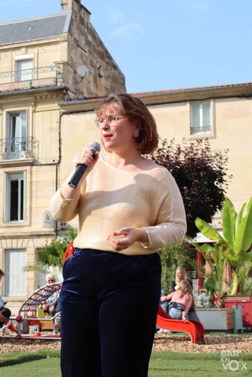 Lydie du groupe Les Chanteuses Anonymes, chante sur la place Reggio, micro à la main.