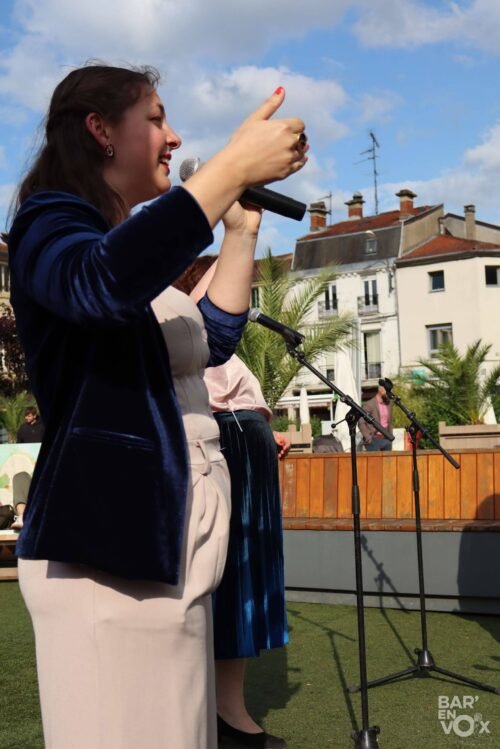 Clara du groupe Les Chanteuses Anonymes, micro à la main, chante en levant la main
