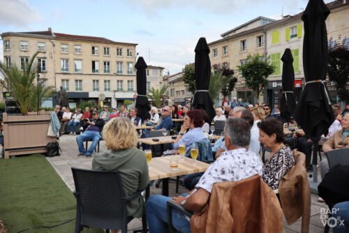 Le public, assis à des tables sur la place Reggio écoute le concert des Chanteuses anonymes.