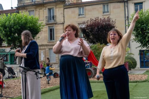 Les chanteuses anonymes, Clara regarde sur le côté, Anne chante micro à la main et, à droite, Lydie lève le bras gauche.