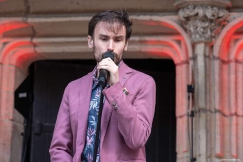 Lorenzo, vêtu d'un blazer mauve, chante en tenant le micro