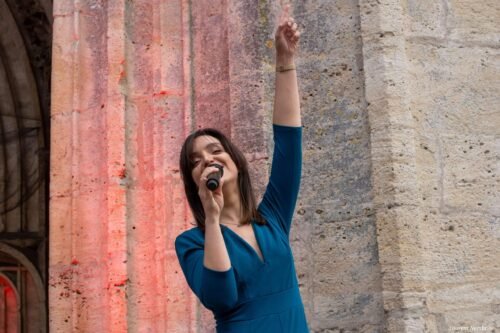 Giulia, chante, micro à la main en levant le bras gauche