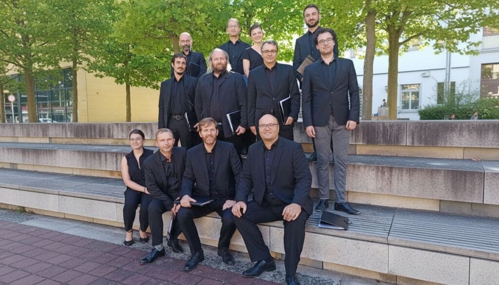 12 chanteurs assis sur des marches devant des arbres