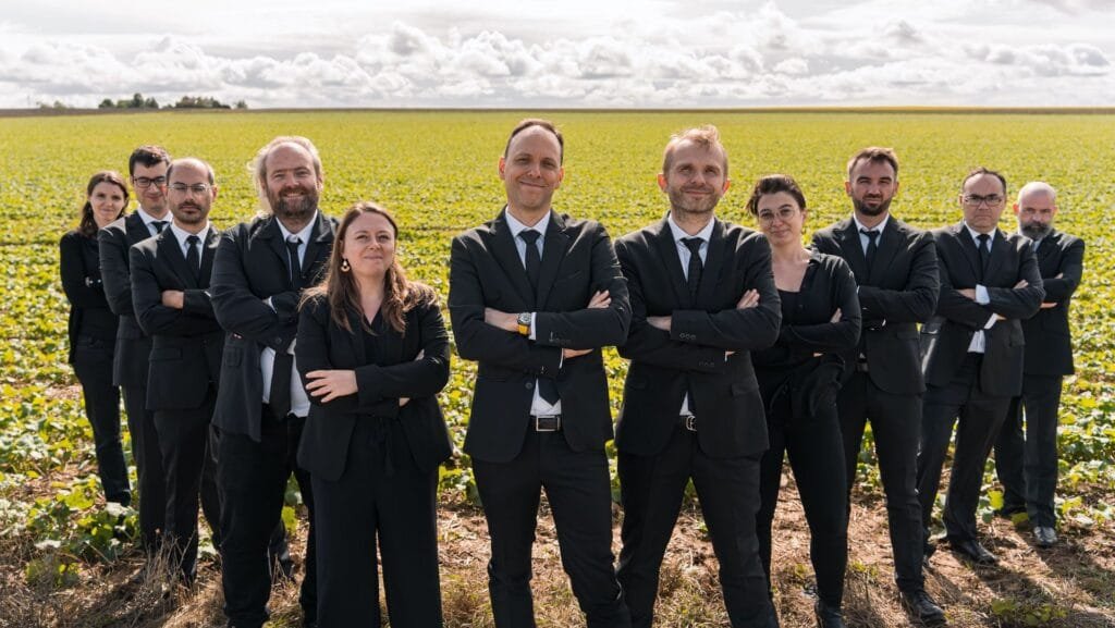 12 chanteurs de VoxpoP posent devant un champ et un ciel nuageux