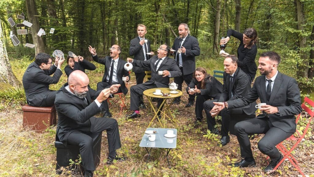 Les 12 chanteurs de VoxpoP, assis autour d'une table dans la forêt, s'amusent.