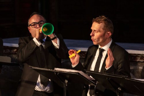 deux chanteurs, l'un joue une trompette en plastique